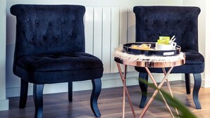 Ein Zimmer mit zwei schwarzen Samt-Sesseln, einem kleinen runden Tisch mit Kupferfuß und einem farbenfrohen, abstrakten Gemälde an der Wand.
