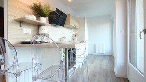 Eine moderne Küche mit einer Holzarbeitsplatte, einem eingebauten Ofen und einer Kaffeemaschine. Zwei Stühle mit transparenten Rückenlehnen und ein Topfpflanze stehen auf der Arbeitsfläche.