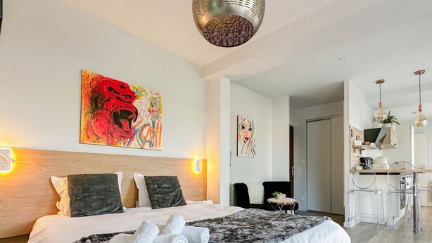 Ein modernes Hotelzimmer mit einem großen Bett, einem kleinen runden Tisch und einer Küchenzeile.