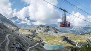 Un téléphérique dans une région montagneuse, avec un ciel dégagé et un lac au premier plan.