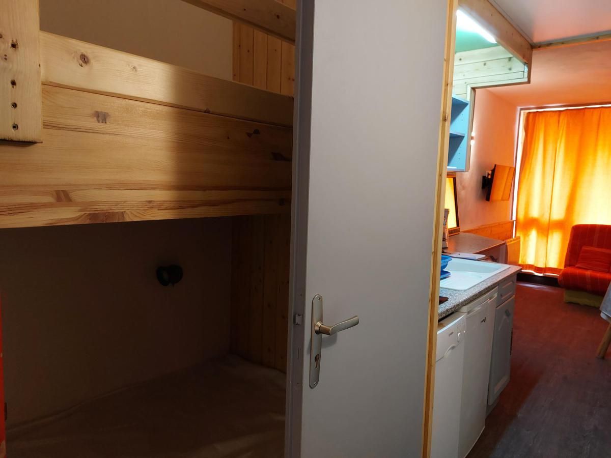 A compact room with a bunk bed, a small kitchenette, and a red chair.