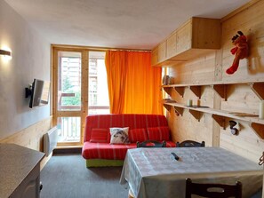 A cozy room with a red sofa, a small table, and wooden shelves.