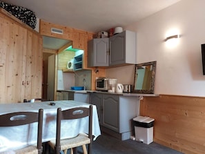 A compact kitchen with a dining area, wooden walls, a microwave, a kettle, and a trash bin.