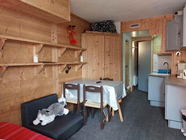 A cozy cabin-style room with a dining table, chairs, a sofa, and a kitchen area with a sink and cabinets.