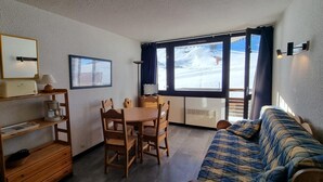 A cozy room with a wooden dining table and chairs, a sofa, and a large window with a view of a snowy landscape.