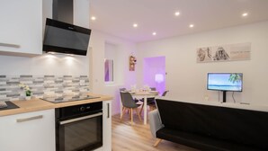 A modern kitchen with a built-in oven and a dining area with a black couch and a TV. - Cosmo incroyable idéal famille rue Carnot (Annecy)