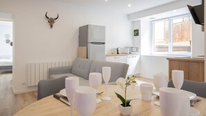 A modern kitchen with a grey refrigerator, white cabinets, and a window with a view of a wooden fence. - Cosmo incroyable idéal famille rue Carnot (Annecy)