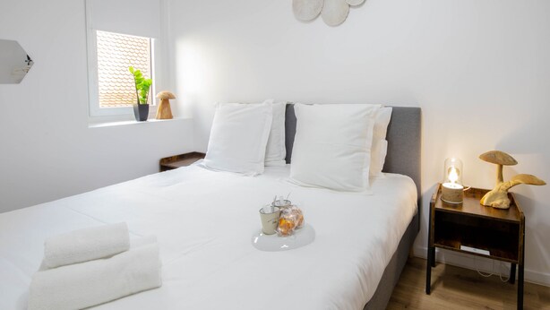 A neatly made bed with white linens, a bedside table with a lamp, and a window with a plant. - Cosmo incroyable idéal famille rue Carnot (Annecy)