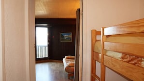 Een kamer met een houten stapelbed, een schilderij aan de muur en uitzicht op een balkon met een leuning.