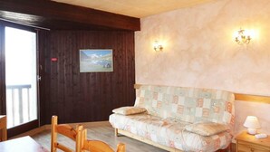 Een gezellige kamer met een houten vloer, een gestreept sofa, een houten stoel, een klein nachtkastje met een lamp en een schilderij aan de muur.