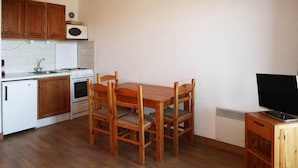 Een kleine keuken met houten kastjes, een magnetron, een fornuis, een spoelbak en een eettafel met stoelen.