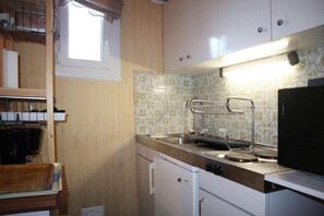 A compact kitchen with a window, a sink with a drying rack, and a refrigerator.