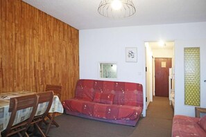 Een kamer met een houten wand, een rode bank, een eettafel met stoelen en een klein raam.
