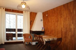 A dining area with a table and chairs, wooden walls, a window with curtains, and a hanging light fixture.