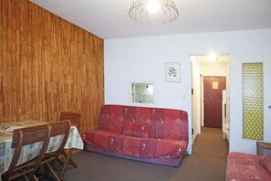 A room with a wooden wall, a red sofa, a dining table with chairs, and a small window.