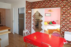 A compact room with a kitchenette, a bed with colorful pillows, and a red table.