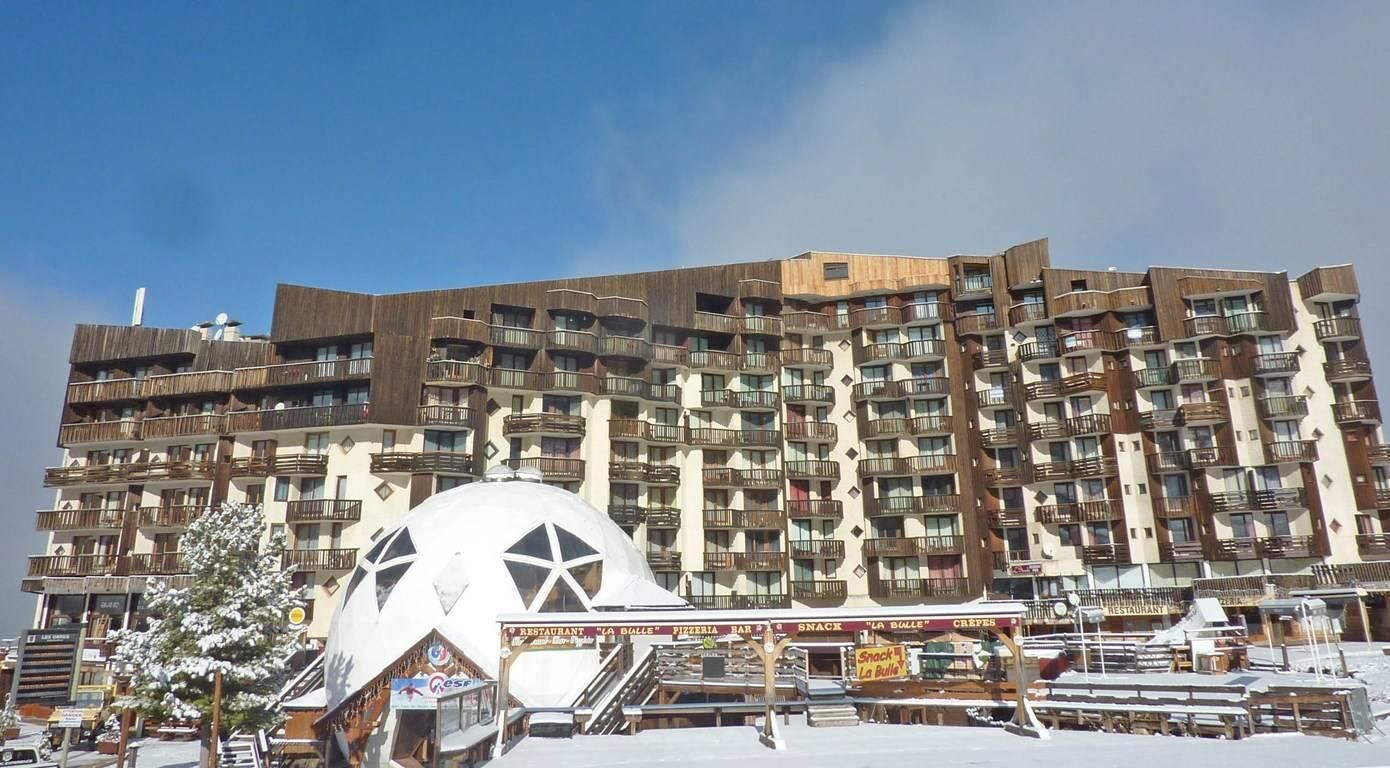 Un hôtel à plusieurs étages, doté de balcons, avec une grande structure en forme de dôme blanc en premier plan.
