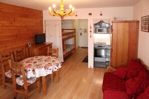 A cozy room with a wooden bunk bed, a dining table with chairs, a red sofa, a chandelier, and a kitchenette.