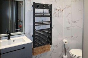 A bathroom with a black towel rack, a white sink, a mirror, and a toilet.