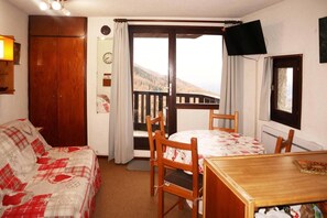 A cozy room with a bed, a dining table, chairs, a balcony with a view, and a TV mounted on the wall.