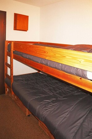 A bunk bed with two levels, a wooden headboard, and a small wooden cabinet on the wall.