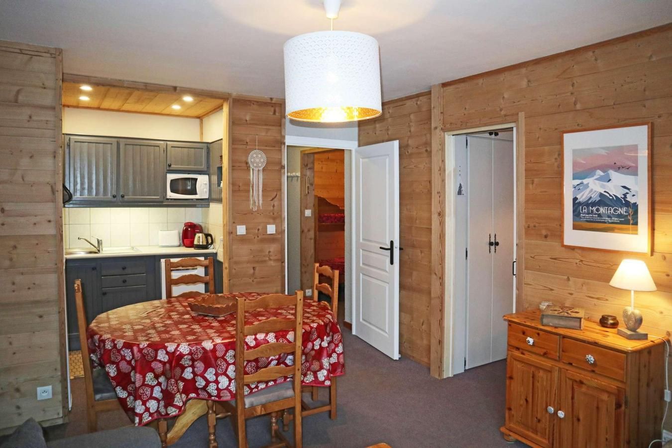 A compact room with a dining table, chairs, a kitchen area, and a wooden cabinet.