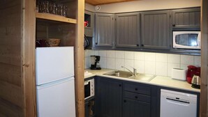 Une cuisine compacte avec des meubles gris, un réfrigérateur blanc, un four à micro-ondes, une machine à café et un lave-vaisselle.