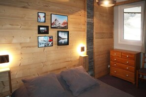A bedroom with a bed, a dresser, a window, and wall-mounted pictures.