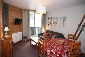 A cozy room with a wooden wall, a sofa, a dining table with chairs, a TV mounted on the wall, and a window with curtains. - Ski-in/ski-out & foot of the slopes, 4th floor, view ski slopes, balcony, tv, 40m², Les Orres (Les Orres)