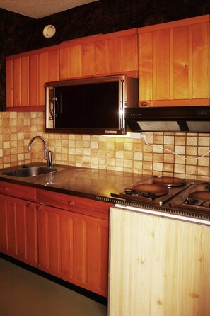 Una cocina con armarios de madera, un lavamanos de acero inoxidable, un microondas y una estufa.