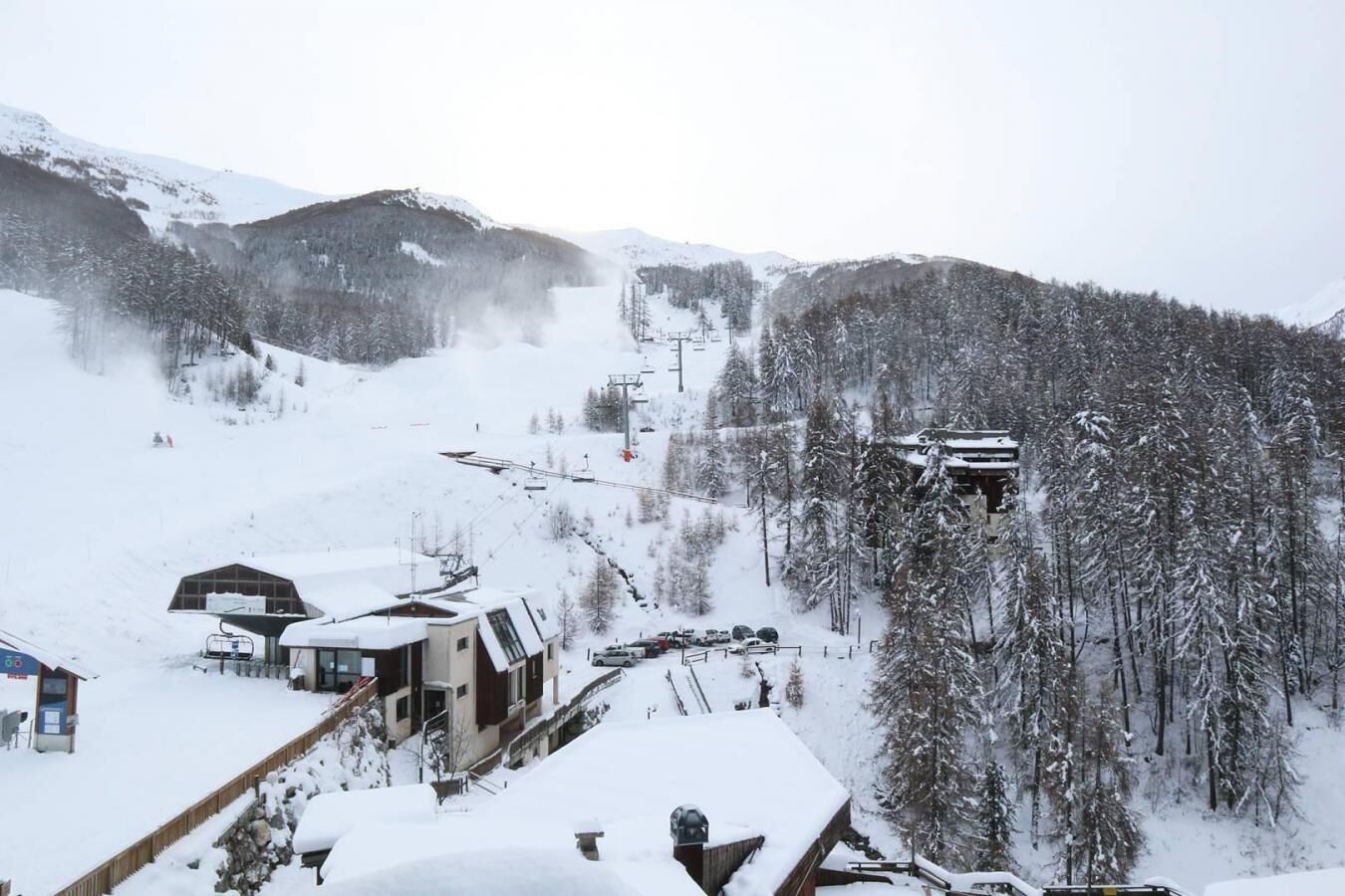 A snow-covered mountain resort with ski lifts, buildings, and a forested area.