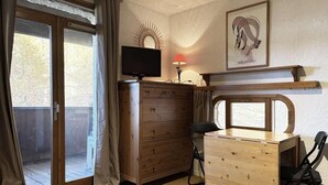 A room with a sliding glass door leading to a balcony, a wooden dresser, a desk with a chair, a television on top of the dresser, and a framed artwork on the wall. - Ski-in/ski-out & foot of the slopes, 4th floor, view valley, balcony, tv, 18m², Les Orres (Les Orres)