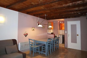 A dining area with a wooden ceiling, a table with chairs, and a kitchenette in the background.