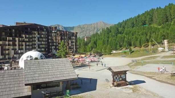 A modern building with multiple balconies, a small kiosk, and a clear view of a mountainous landscape. - Ski-in/ski-out & foot of the slopes, 4th floor, view ski slopes, balcony, tv, 22m², Les Orres (Les Orres)