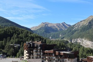 A modern multi-story building with balconies, set against a backdrop of forested mountains.