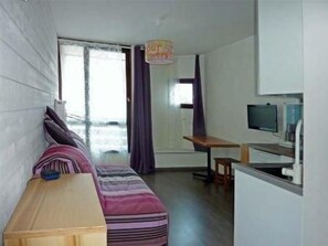 A compact room with a bed, a small desk, a television, and a window with curtains.
