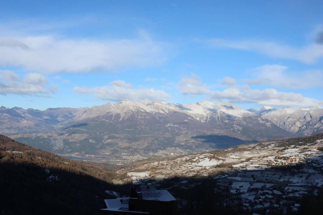 Un paysage montagneux aux sommets enneigés, une vallée parsemée de bâtiments et un ciel dégagé.