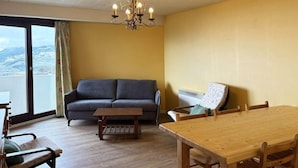 A living room with a sofa, a dining table, and a view of a cityscape through large windows.
