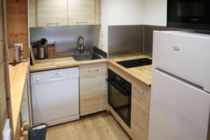 A compact kitchen with a dishwasher, oven, sink, and a refrigerator.