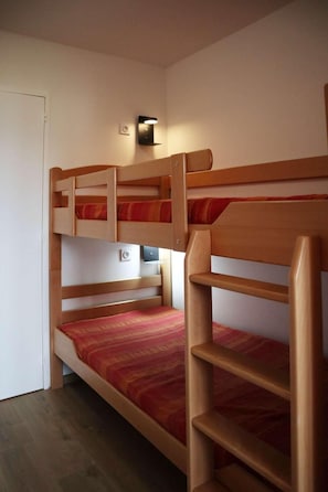 A bunk bed room with a wooden frame, a small shelf, and a wall-mounted light fixture.