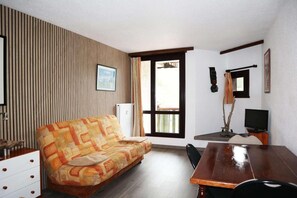 A room with a sofa, a dining table, a TV, and a window with curtains.