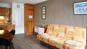 A cozy room with a wooden dining table, a sofa, and a kitchen area with wooden cabinets and a clock on the wall.