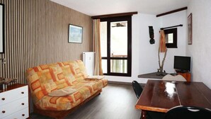 A room with a sofa, a wooden table, a TV, and a window with curtains.
