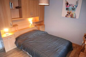 Een slaapkamer met een bed, houten kastjes, een bureau en een lamp.