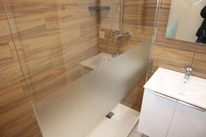 Een moderne badkamer met een douchecabine van glas, een wit wastafelmeubel en houten wandtegels.