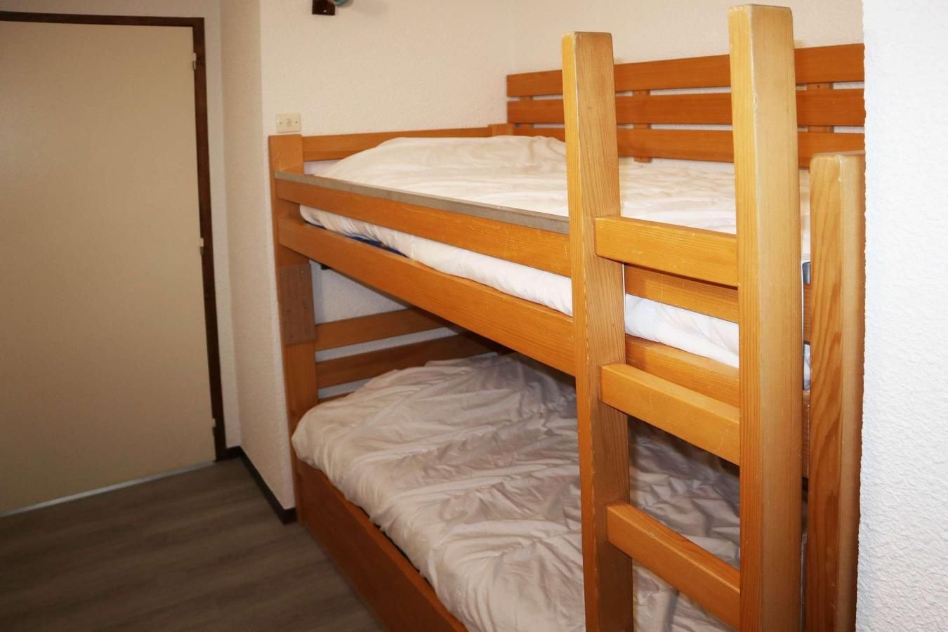 A bunk bed with two levels, wooden headboards, and white bedding.