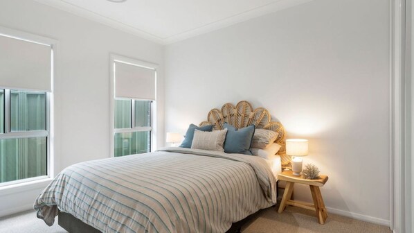 A bedroom with a large bed, a bedside table with a lamp, and a window with curtains. - Gone Coastal at Narrawallee (Narrawallee)