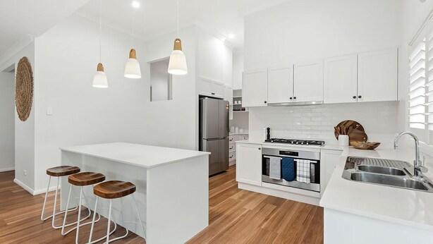 A modern kitchen with white cabinetry, a central island with stools, a stainless steel refrigerator, and a built-in oven. - Gone Coastal at Narrawallee (Narrawallee)