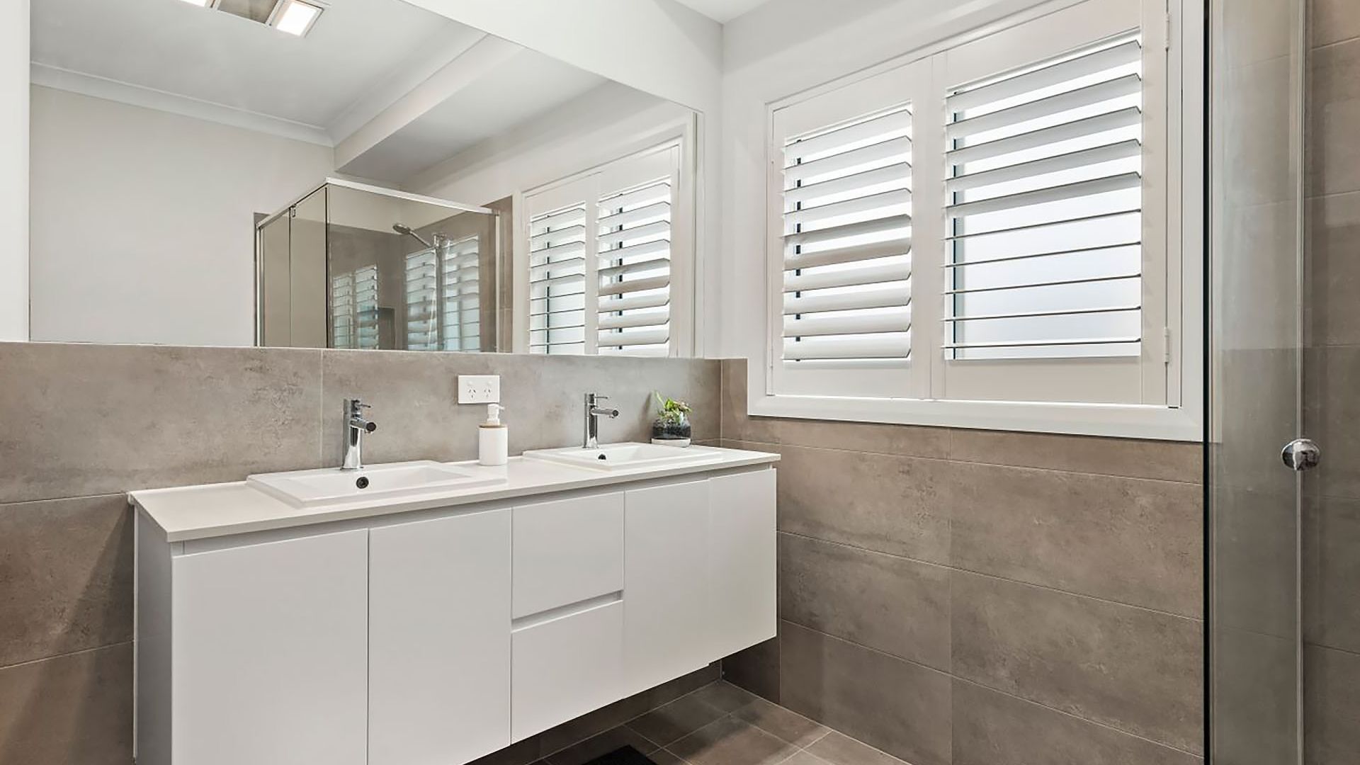 Un baño moderno con tocador doble, un espejo grande y zona de ducha.