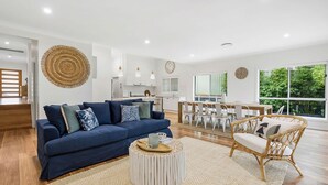 A modern living room with a blue sofa, a round coffee table, and a wicker chair. - Gone Coastal at Narrawallee (Narrawallee)